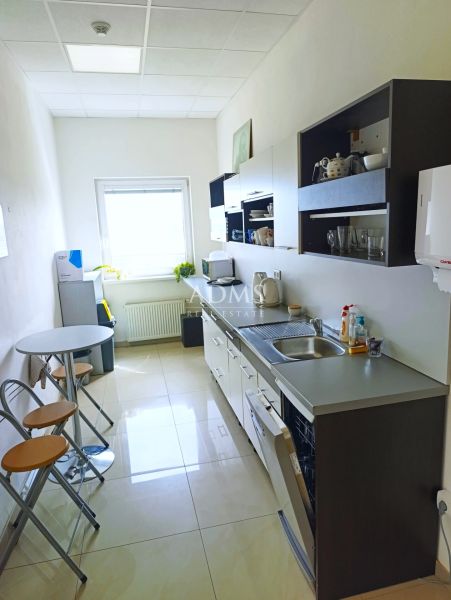 The kitchen in the offices with white walls, a sink, and a table with chairs.