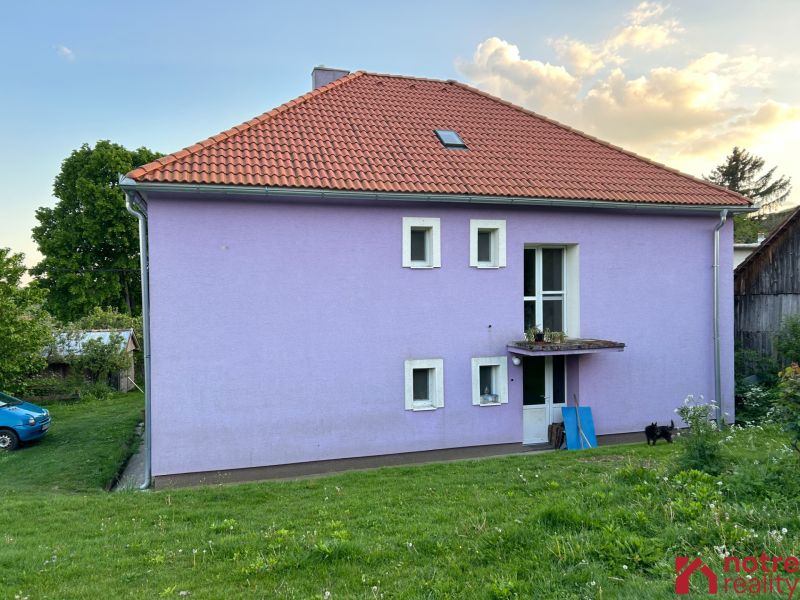 A family house in Kosihovce with a purple facade and a red roof on a grassy plot.