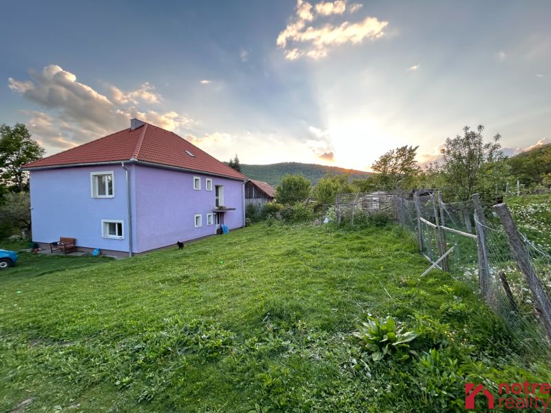 A family house in Kosihovce surrounded by a garden, with mountains and a setting sun in the background.