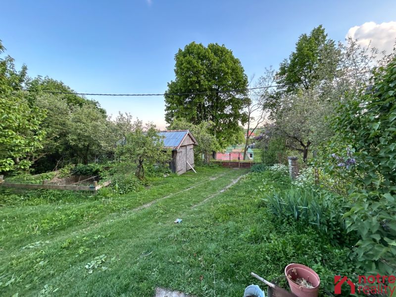 The garden of a family house in Kosihovce with a lawn, trees, and a small wooden structure.