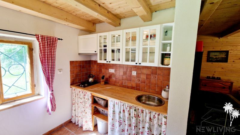 A kitchen in a cottage with white cabinets, ceramic tiles, and a wooden ceiling.
