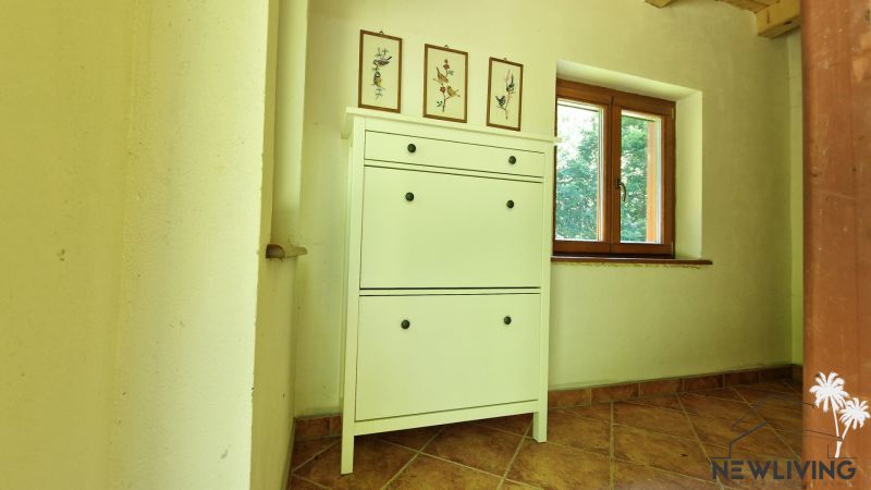 White cabinet with decorations, next to a wooden window, floor tiles behind the cottage.