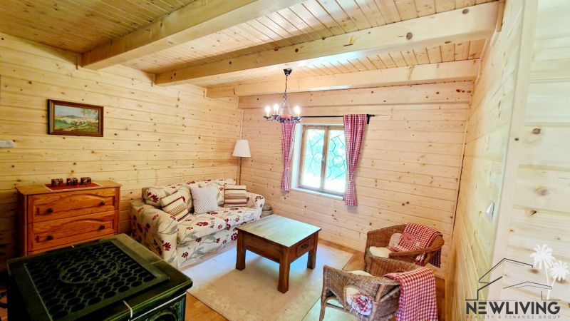 A wooden interior of a cabin with a stove, a sofa, and rattan chairs.