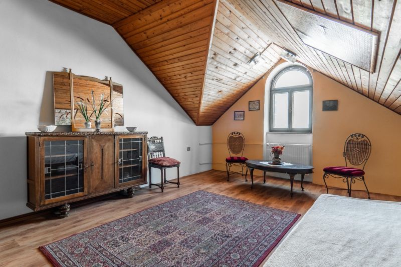 Attic with wooden paneling, antique furniture, wooden decor flooring, decorative carpet.