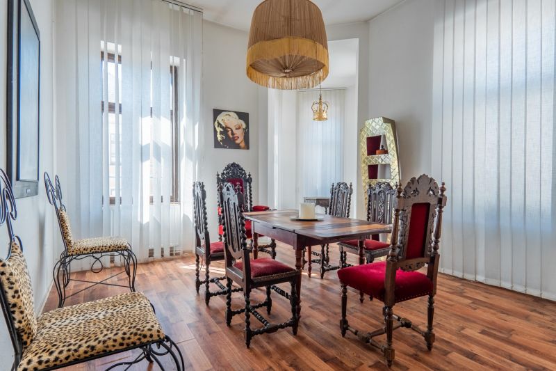 Dining room in a cottage with decorated chairs and a wooden-patterned floor.