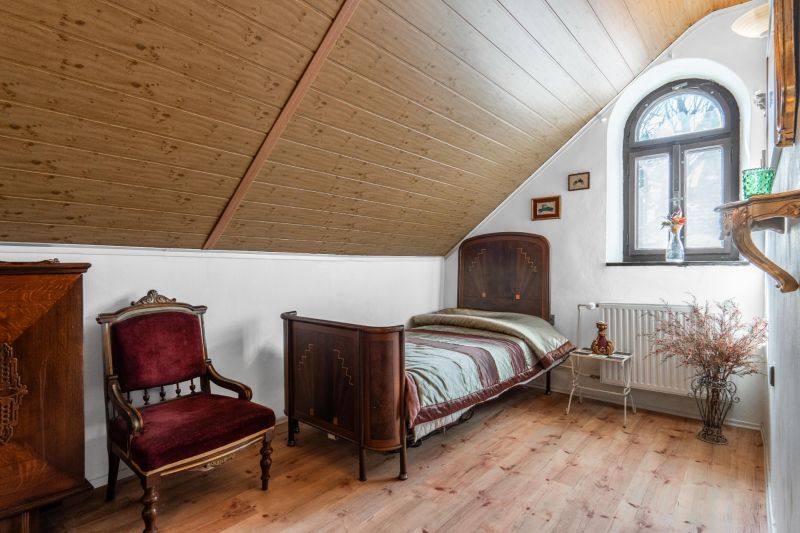 A room in a cottage with wooden decor, antique furniture, a bed by the window.