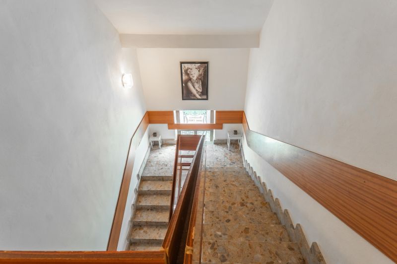 A staircase in a cottage with a portrait on the white wall, stone steps, wooden railing.