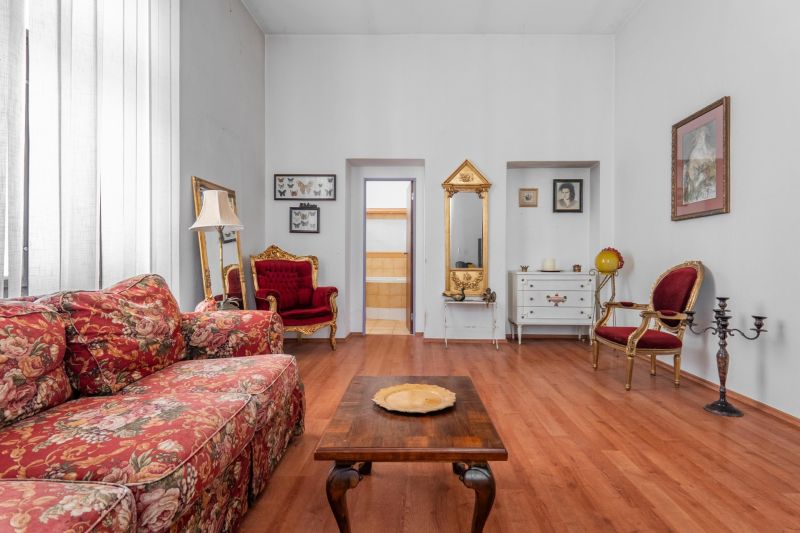 Interior of a cottage with a floral sofa, decorative chairs, and a wooden-patterned floor.