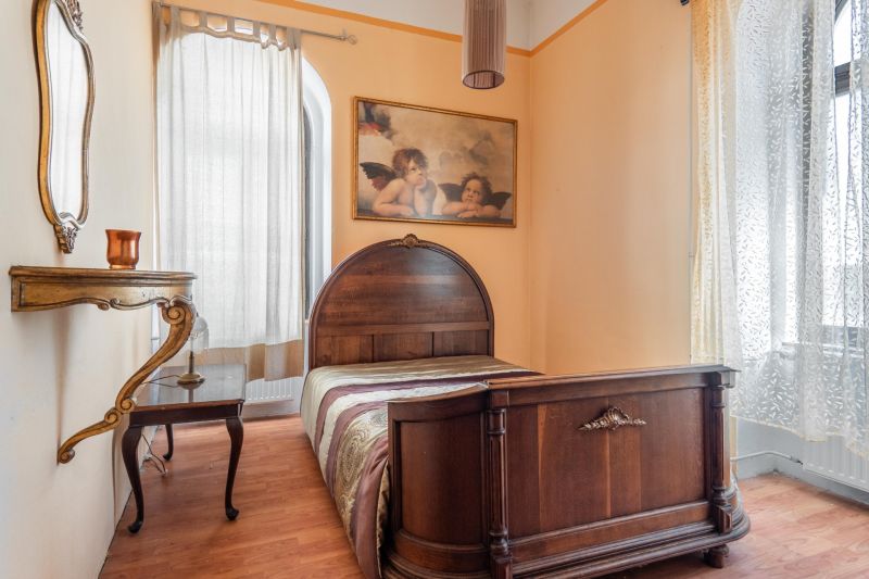 A room in a cottage with a bed, a mirror, a painting, and a floor with a wooden decor.