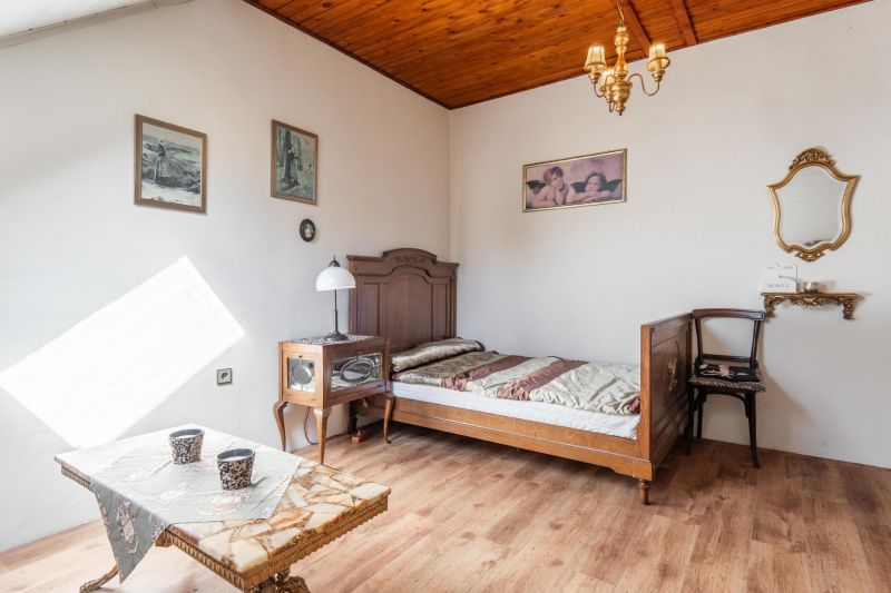 The interior of a cabin with wooden floor decor, a simple bed, and an antique chair.