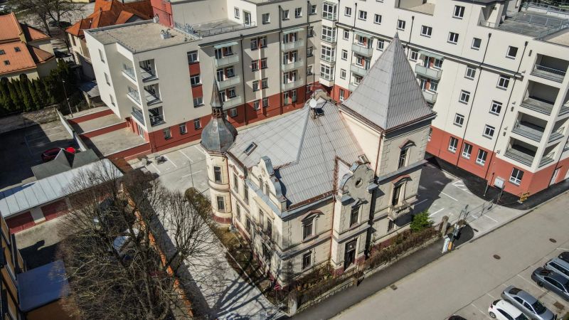 A historical building surrounded by modern apartment buildings on Hviezdoslavova Street in Trenčianske Teplice.