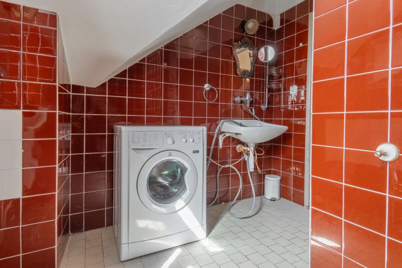 A bathroom in a cottage with red tiles, a washing machine, and a sink.