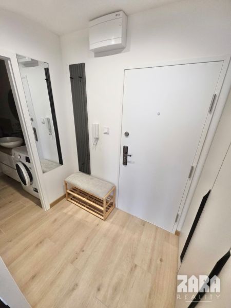 Interior of a 2-room apartment with a wooden decor floor, a bench, and entrance doors.