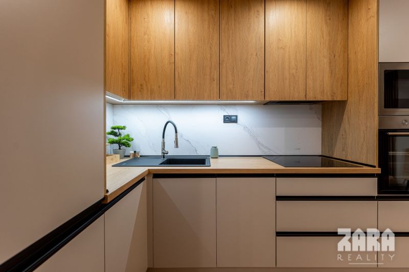 A kitchen in a 2-room apartment with a wooden decor floor and built-in appliances.