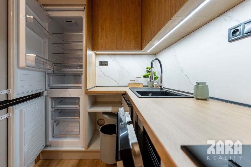A kitchen in a 2-room apartment with a wooden decor floor and built-in appliances.