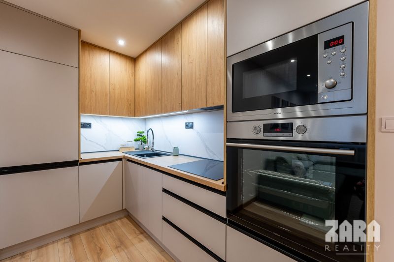 A kitchen in a 2-room apartment with a wood-patterned floor and built-in appliances.