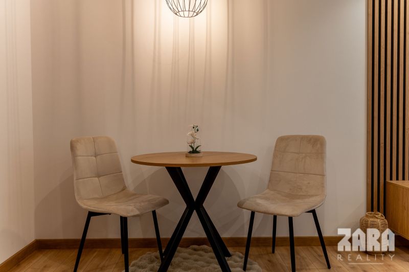 Dining nook in a two-room apartment with a wood-patterned floor and a round table.