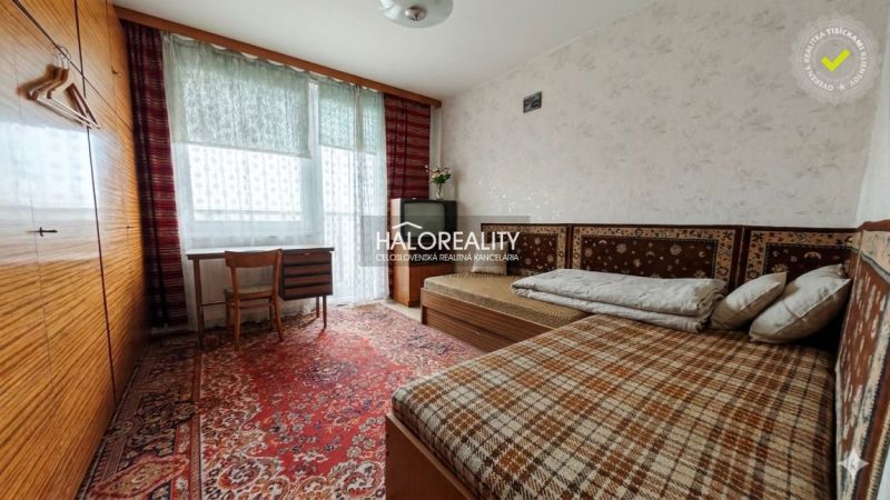 A room in a 4-room apartment with a carpet, two beds, and a writing desk.