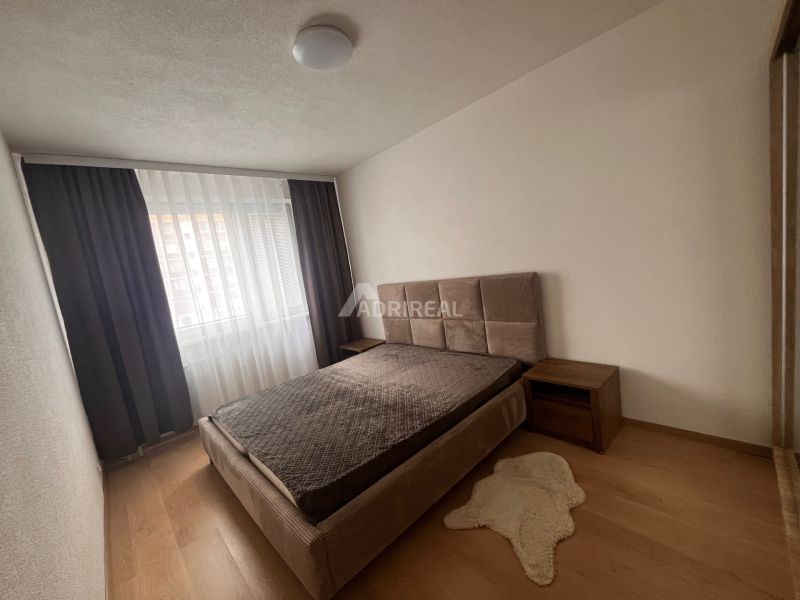 A bedroom in a 2-room apartment with a wooden decor floor and a bed by the window.