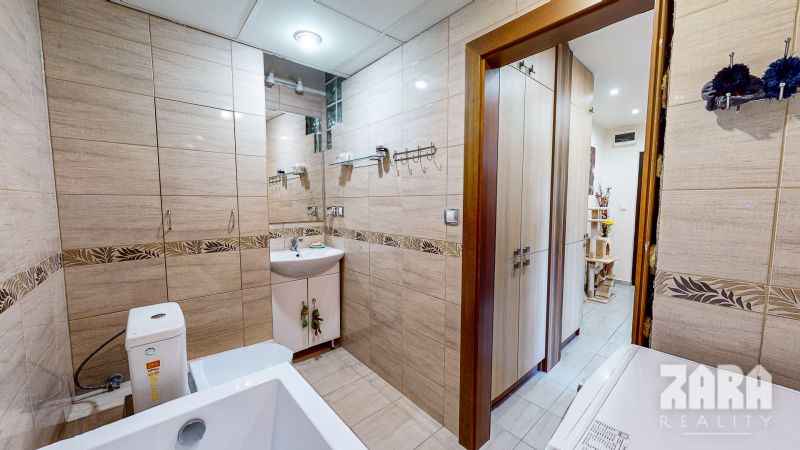 Bathroom of a three-room apartment with light tiles and a mirror.