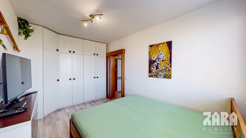 A bedroom with white furniture, a picture of a leopard, a television, and a wooden decor floor.