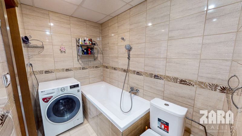 Bathroom in a 3-room apartment with a bathtub, washing machine, and toilet, in ceramic tiles.
