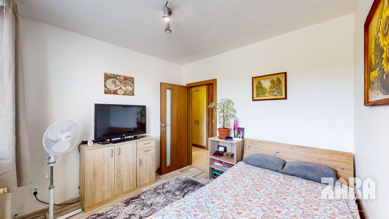 A bedroom in a 3-room apartment with a television, pictures, and a plant on the dresser.