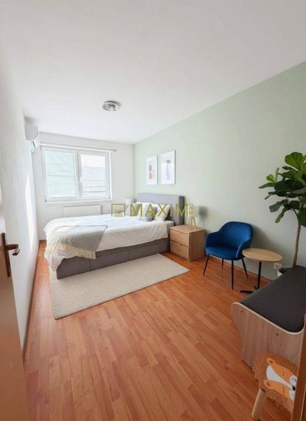 A bright bedroom with a bed, wood-patterned flooring, and furniture in a two-room apartment.