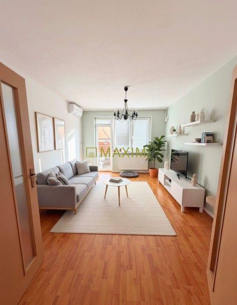 Living room in a two-room apartment with a wooden decor floor, a sofa, and a television.