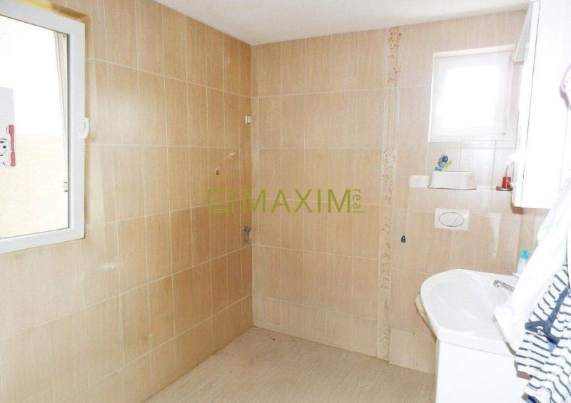 A bathroom in a cottage with beige tiles and a window letting in natural light.