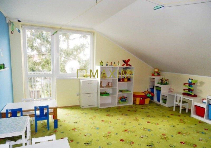 A children's playroom with a colorful carpet and tables full of toys and shelves in a cottage.