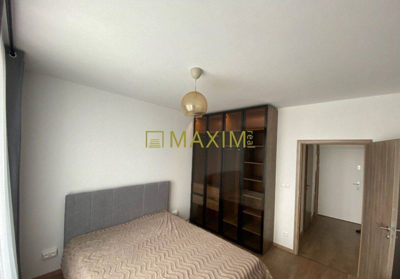 A bedroom in light shades with a bed, wardrobe, and wooden decor flooring.