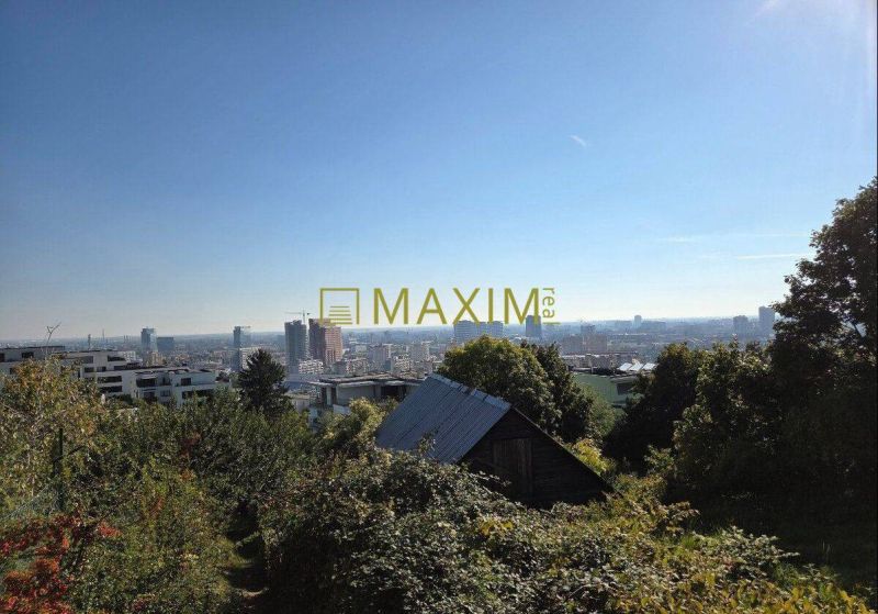 View of Bratislava from the plot on Tupého, green trees, buildings in the background.
