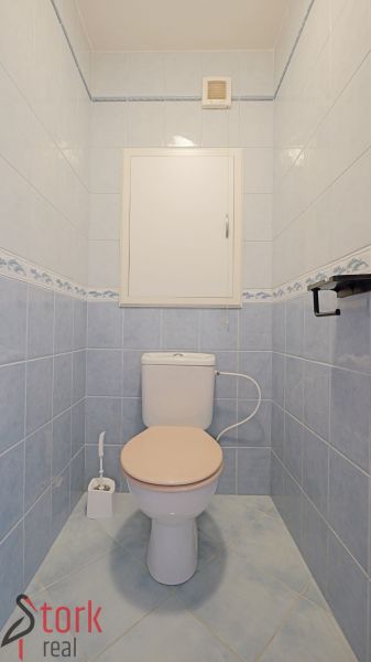 A toilet with light blue tiles, a white toilet, and space for cleaning products.