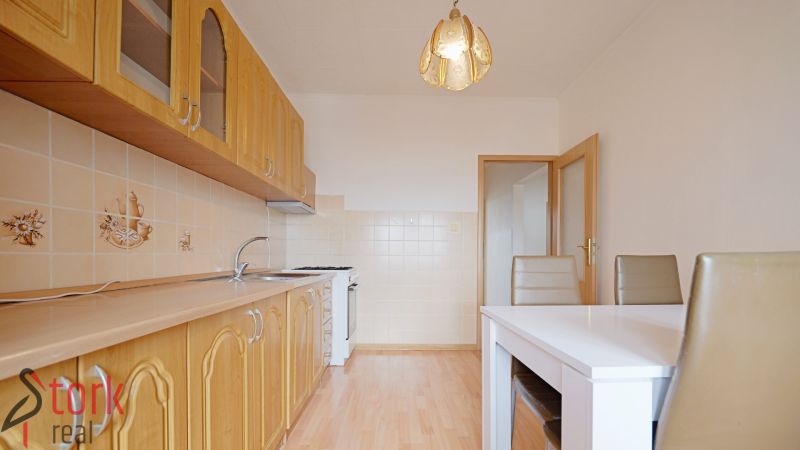 A kitchen with a wooden countertop, a floor with a wooden decor, a dining table, and chairs in a 3-room apartment.