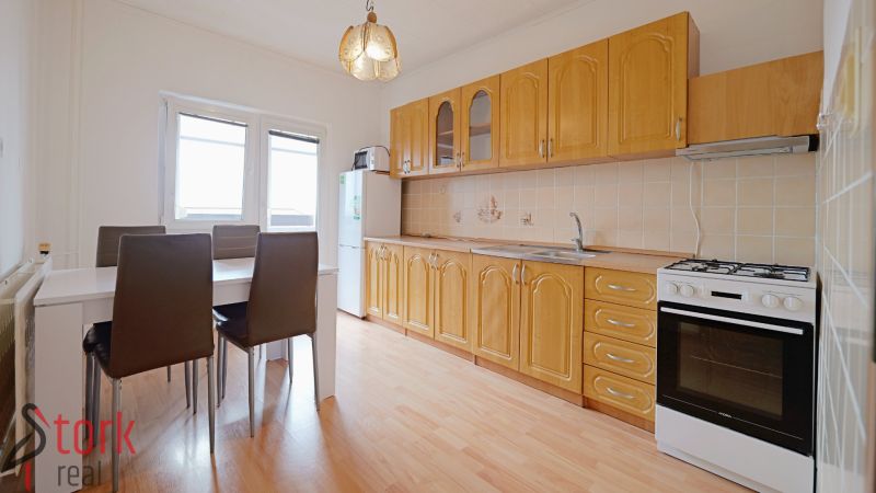 A kitchen in a 3-room apartment with a kitchen unit, dining table, and a floor with a wooden decor.