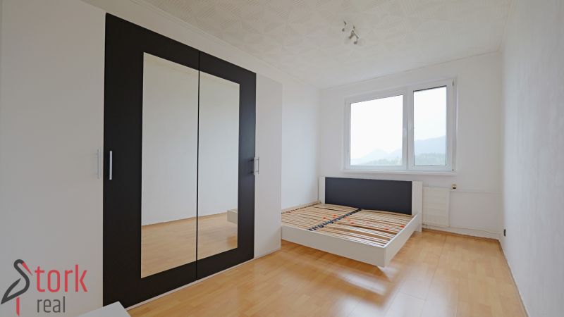 A bright bedroom with a bed and a wardrobe, a floor with a wooden decor in a 3-room apartment.