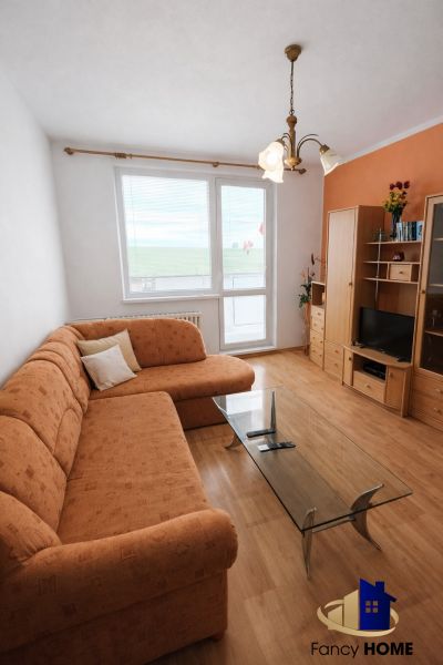 A living room in a two-room apartment with an orange sofa and a wooden-patterned floor.