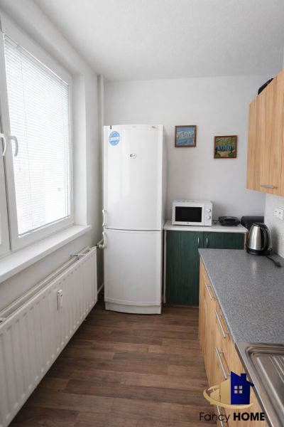 Kitchen in a 2-room apartment with a refrigerator and kitchen unit, floor with wooden decor.