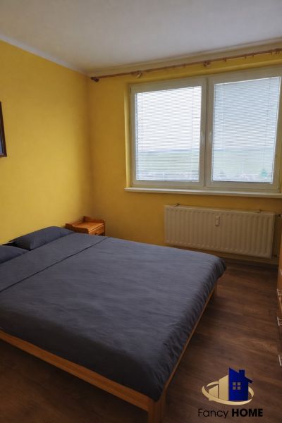 Bedroom in a 2-room apartment with a bed, yellow walls, and a wood-patterned floor.