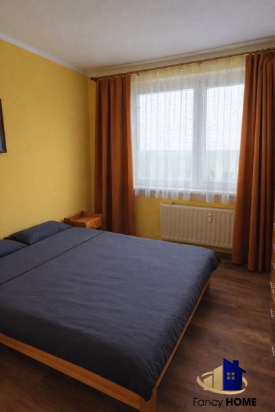 A bedroom in a two-room apartment with a wooden decor floor and orange curtains.