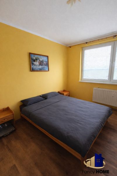 A bedroom in a two-room apartment with a wooden decor floor and yellow walls.