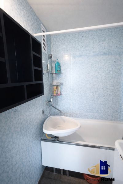 Bathroom in a 2-room apartment with a bathtub, sink, and shelving storage system.