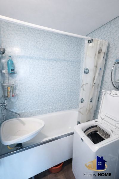 Bathroom in a 2-room apartment with a bathtub and a top-loading washing machine.