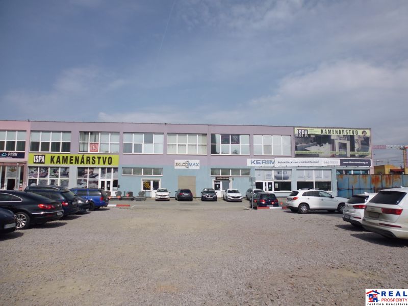 The exterior of commercial premises at Masarykova 22 in Prešov with a parking lot in front of the buildings.