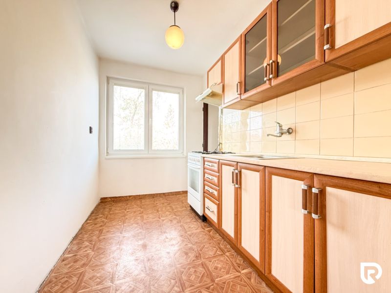 A kitchen with a wooden decor floor in a 3-room apartment with a simple kitchen unit.