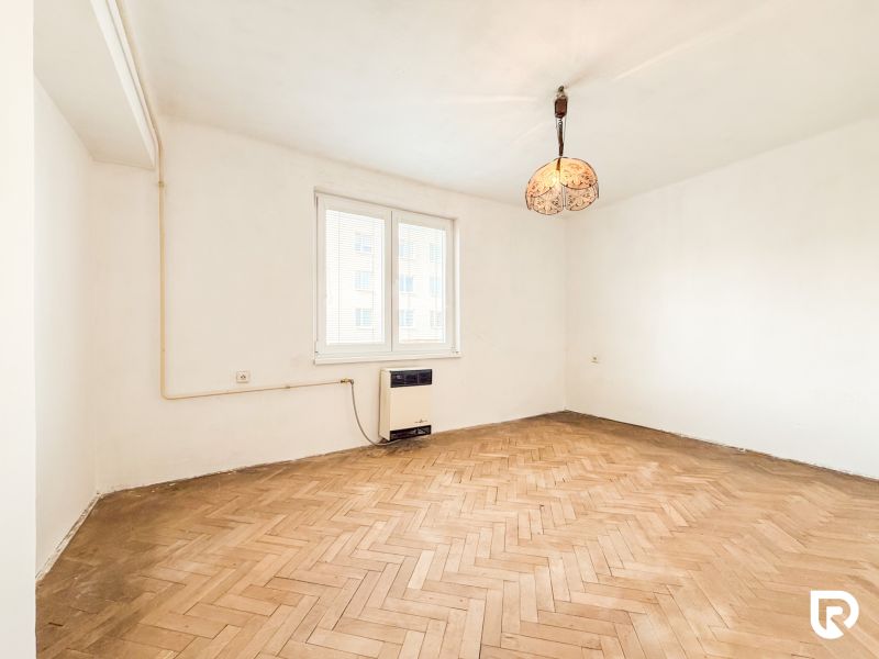 A room with white walls, a floor with a wooden decor, a pendant light in a 3-room apartment.