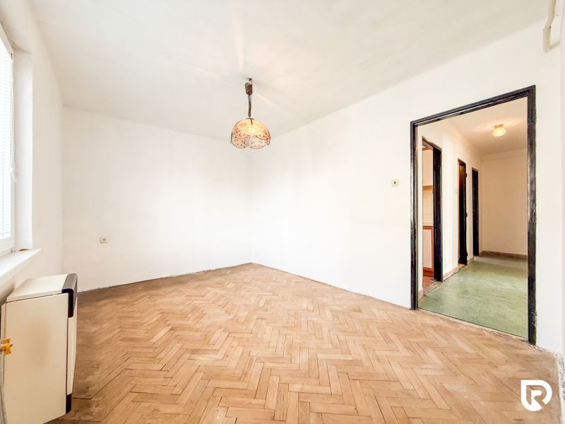 A room in a 3-room apartment with a wooden decor floor and a hanging lamp.