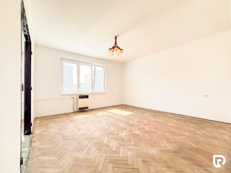 A spacious room with a wooden decor floor and a large window in a 3-room apartment.
