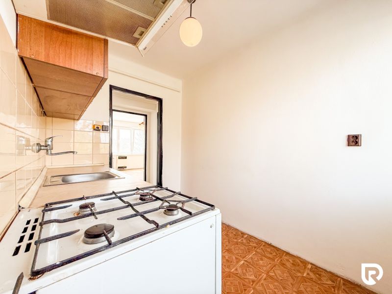 A kitchen in a 3-room apartment with a gas stove and wooden floor decor.